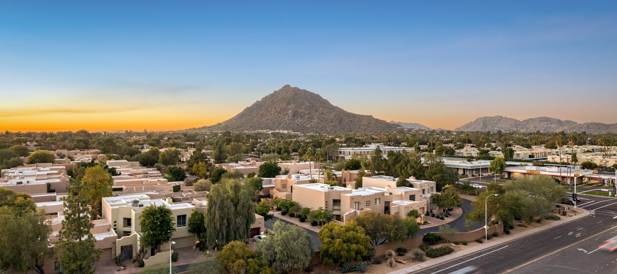 View from Optima Sonoran Village apartment rooftop of suburban neighborhood with desert landscaping and a mountain backdrop at sunset.