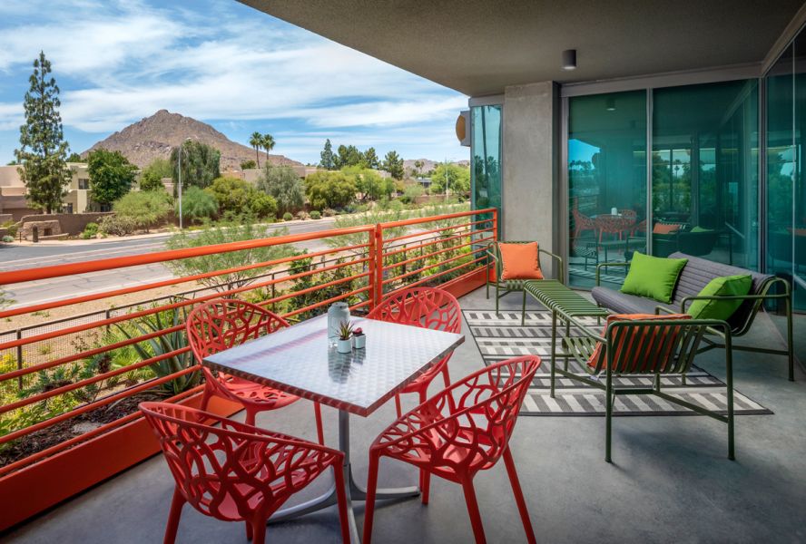 Modern balcony with red chairs, metal table, green cushioned seating, and mountain view in the background at Optima Sonoran Village apartments.
