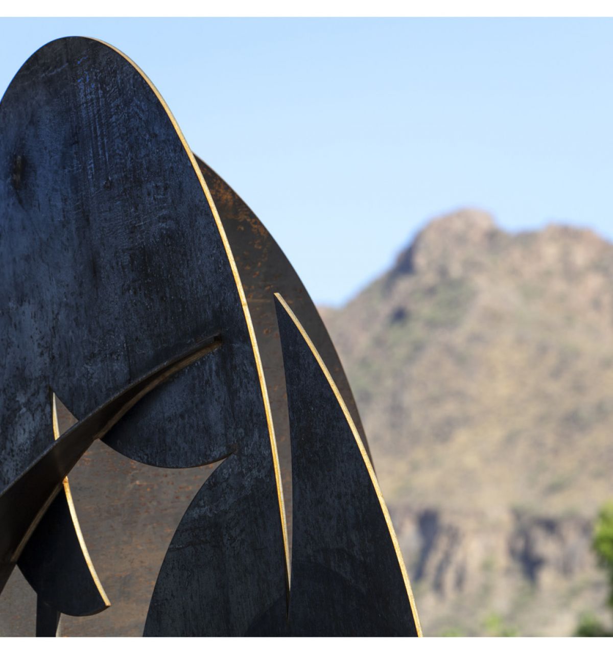 Abstract metal sculpture art set against a mountain and clear blue sky, inspiring creativity in the community.