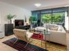 Modern living room at Optima Sonoran Village with white sectional sofa, striped rug, glass wall, and greenery outside.