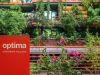 Red "Optima Sonoran Village" sign in front of lush greenery and modern building showcasing sustainable architecture with plants and flowers.
