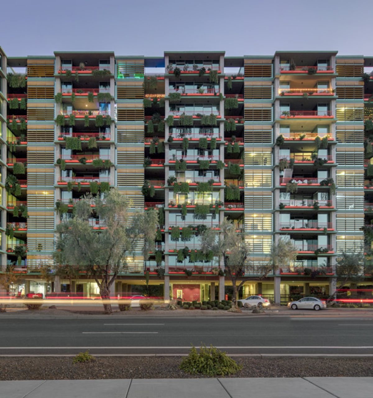 Modern multi-story Optima Community apartment building with balconies, viewed from across a busy street at sunset.
