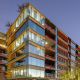 Optima Sonoran Village Modern glass apartment building surrounded by desert landscaping at dusk, with lights on inside.