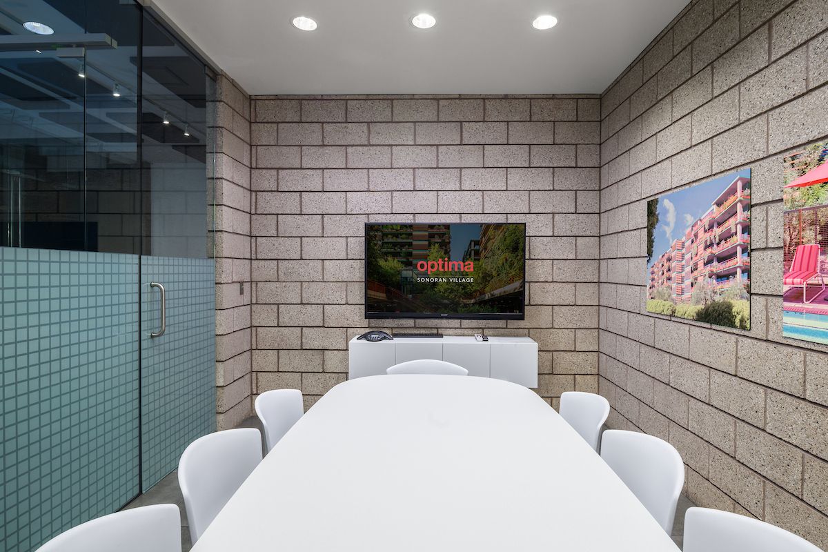 Modern conference room with Optima designs, a white table, chairs, TV, and building photos—ideal for meetings or remote work.