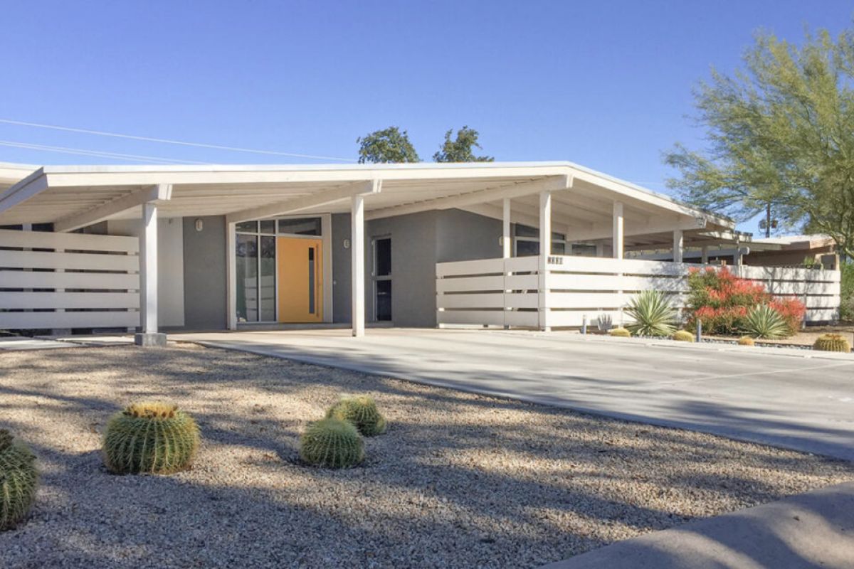 Mid-century modern house inspired by Arizona architect Ralph Haver, featuring a yellow door, carport, and desert landscaping with cactus.