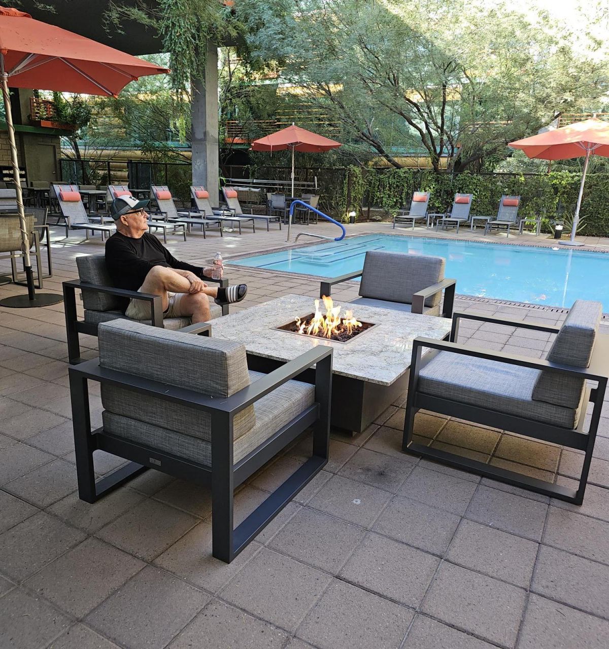 Resident Stories: Bob McMillan enjoys a cozy evening by the fire pit at Optima Sonoran Village with poolside views and orange umbrellas.