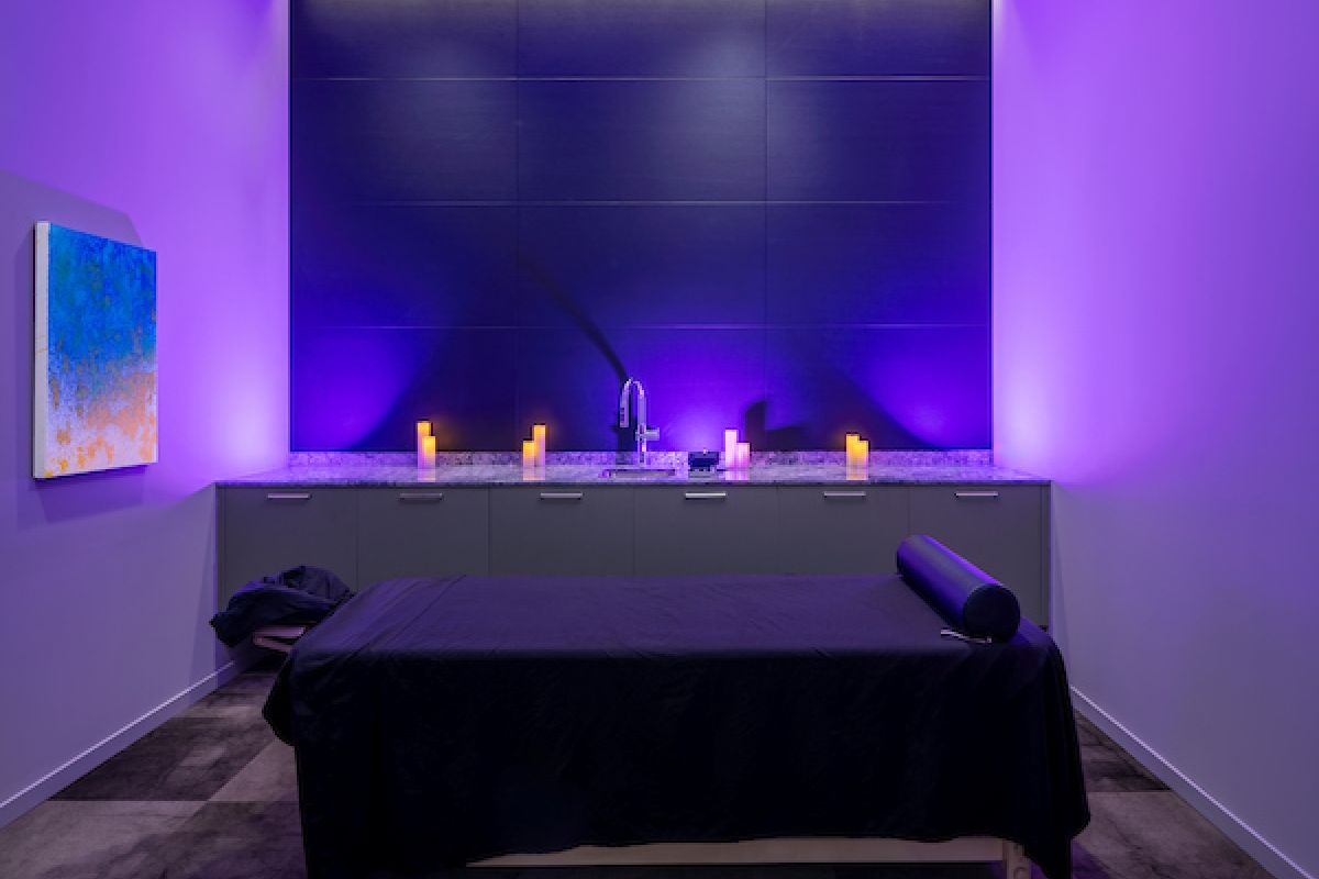 A massage room with purple lighting, a massage table, candles, and abstract art—perfect for experiencing the health benefits of massage therapy.