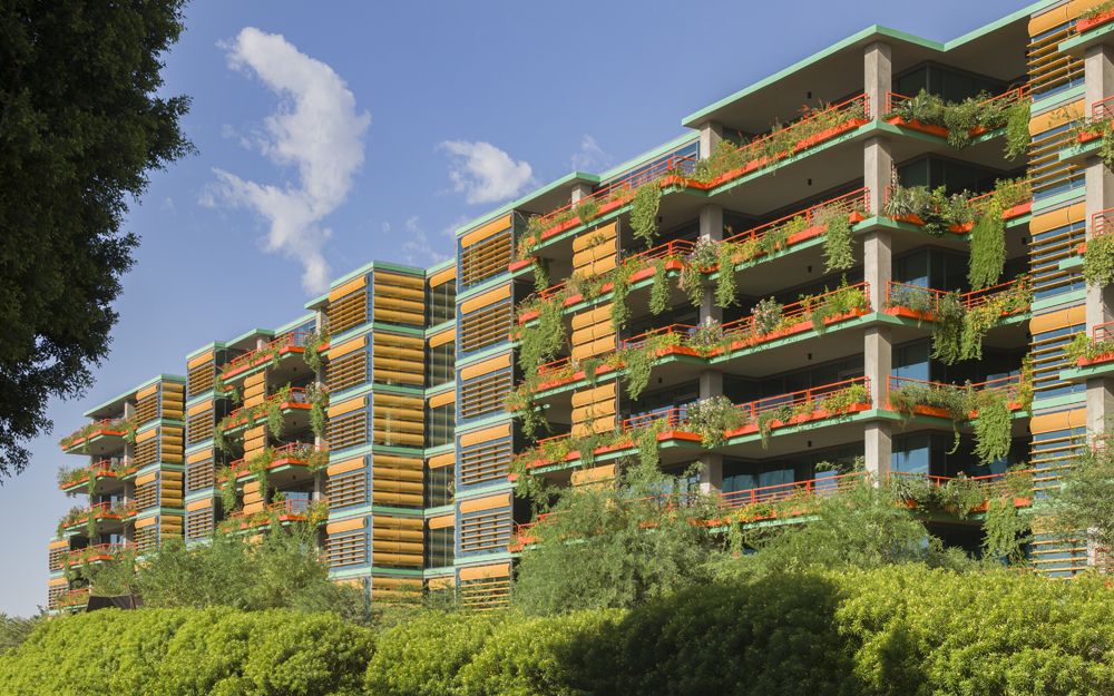 Optima Sonoran Village modern apartment building with colorful accents and lush plants on balconies, under a clear blue sky.