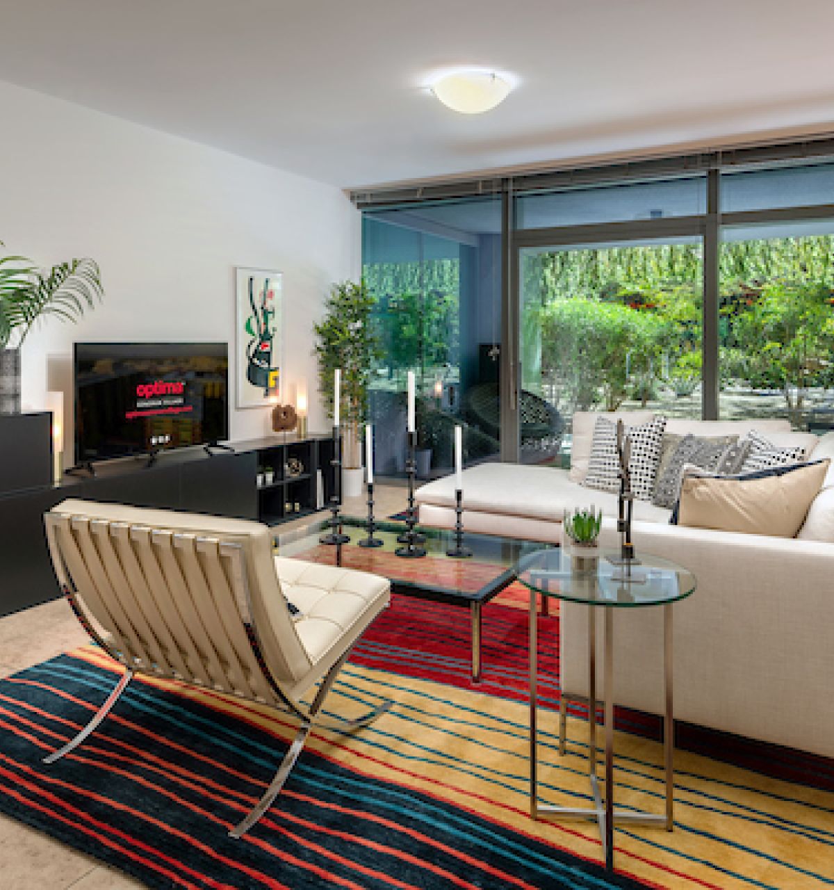 Modern living room at Optima Sonoran Village with white sectional sofa, striped rug, glass wall, and greenery outside.