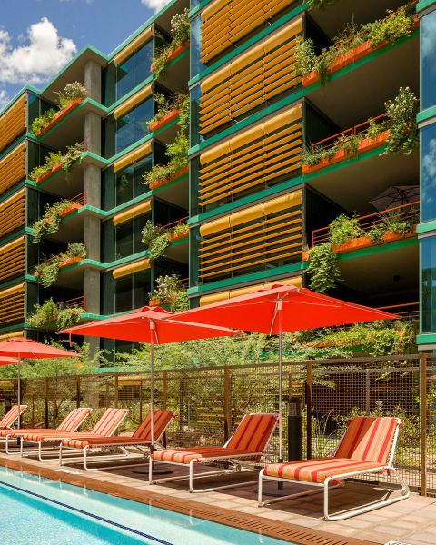 Red sun loungers and umbrellas by a pool and lush landscaping at Optima Sonoran Village apartments.