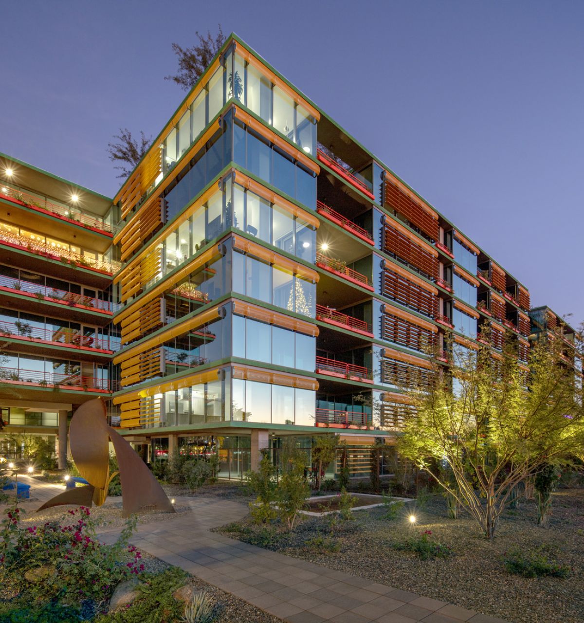 Modern glass and steel building with red accents, a home environment designed to enhance sleep quality, surrounded by desert landscaping at sunset.