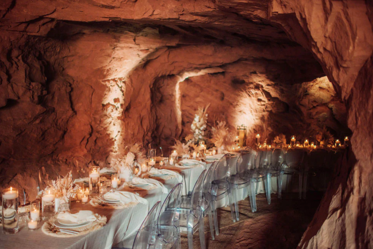 Elegant dinner table set with candles and glass chairs, styled by Cloth and Flame, inside a softly lit, rocky cave.