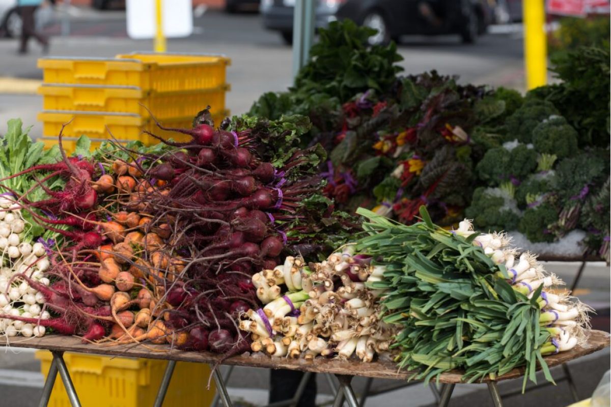 Fresh root vegetables and greens at the Scottsdale Farmers Market, capturing the vibrant local flavor with yellow crates in the background.