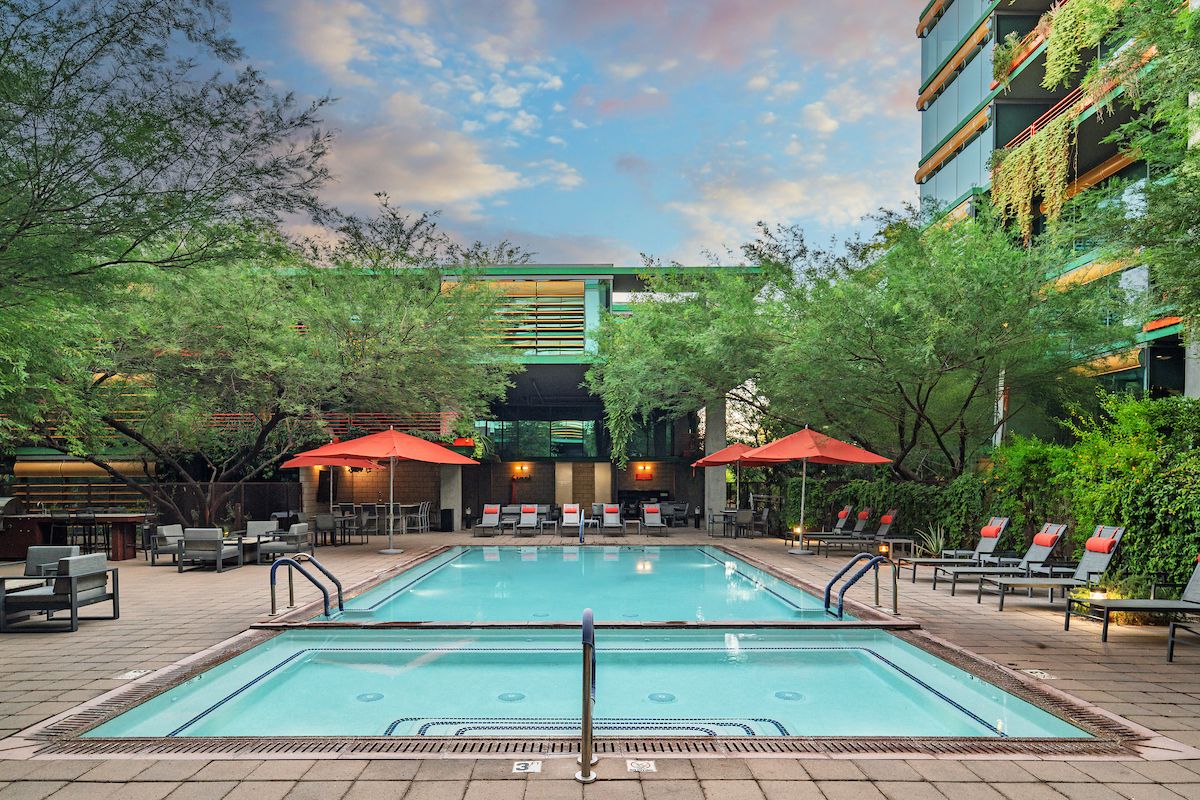 Modern outdoor pool area with lounge chairs and red umbrellas for Optima Residents to relax at sunset—now available to rent.