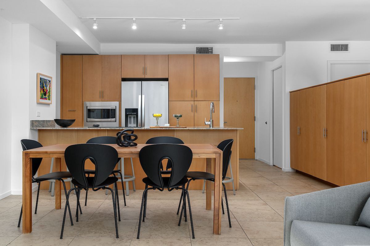Modern Optima kitchen design and dining area with wooden cabinets, black chairs, and neutral tiled flooring for a stylish home.