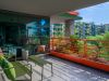 Modern Optima balcony with green metal furniture, orange railing, lush greenery, and buildings in the background enhances your outdoor space.
