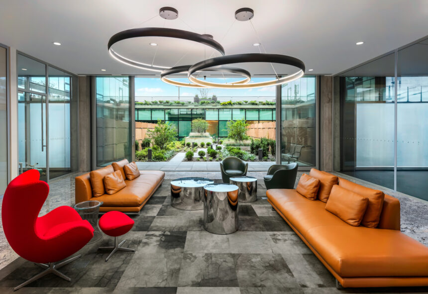 Modern lounge area with tan sofas, red chair, and garden views—a space shaping sustainable futures through thoughtful design.