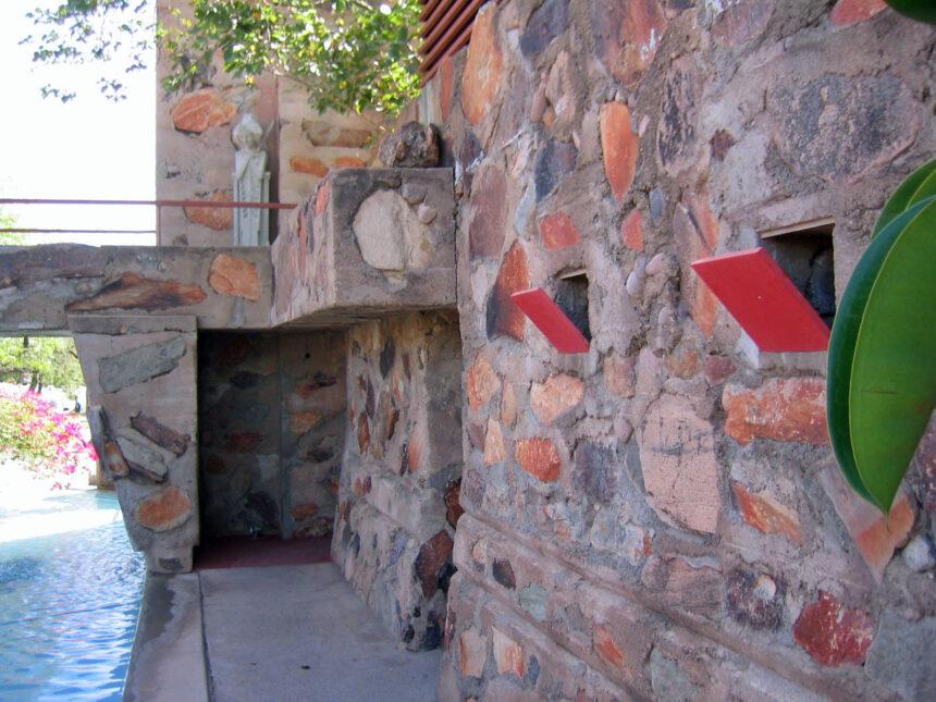 Stone wall with red arrow designs by a poolside path and leafy plant in sunny Scottsdale—perfect for a fall travel guide.