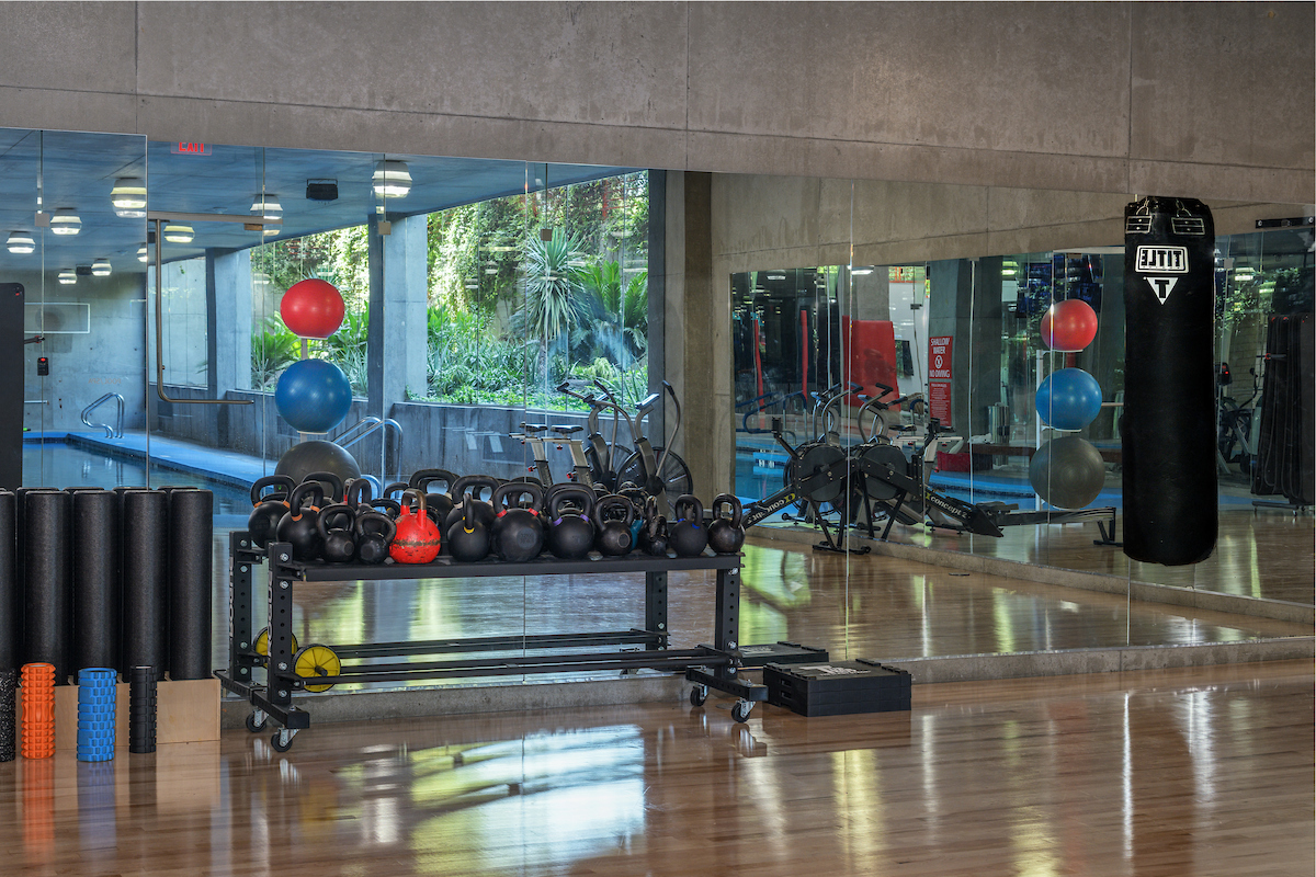 A productive space for daily routines, featuring kettlebells, foam rollers, a punching bag, exercise balls, and a mirrored wall.