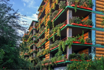Apartment building with green plants and flowers covering the balconies and facade, surrounded by trees.