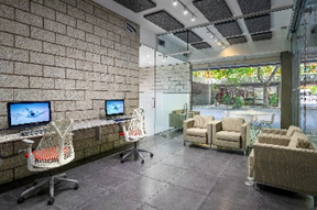 Modern office lounge by Optima designs with two computers, armchairs, glass walls, and a view of greenery—perfect for the way we work today.