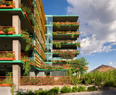 Modern Optima building with green balconies and potted plants, set against a blue sky and distant mountain.