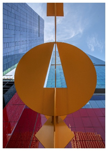 View looking up at colorful modern buildings and a large yellow geometric sculpture against a blue sky.