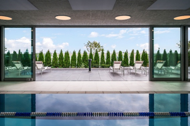 Indoor pool with lounge chairs and greenery, plus Optima Sky Decks’ rooftop amenities and city views through large glass doors.