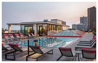 Rooftop pool with lounge chairs, modern building, and city skyline at sunset.
