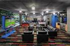 Modern lounge with sofas, colorful carpet, large windows, and TV screens, resembling a stylish meeting space.