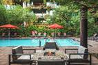 Outdoor pool with lounge chairs, red umbrellas, greenery, and a seating area with a fire pit in front.