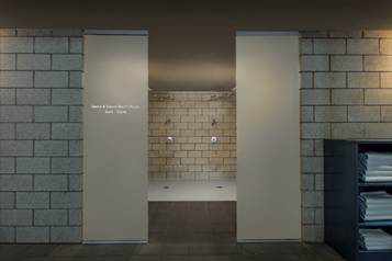 Entrance to a communal shower area with tiled walls and stacked white towels on shelves to the right.