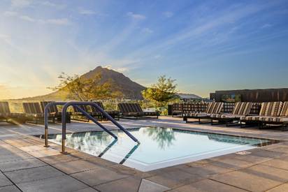 A small outdoor pool with lounge chairs and mountain views at sunset, under a clear blue sky.