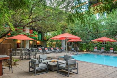 A poolside patio with lounge chairs, tables, red umbrellas, and lush greenery surrounding the area.