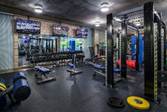 Modern gym with weight benches, racks, dumbbells, mirrors, and various exercise equipment under bright lighting.