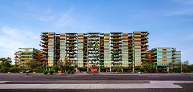 A multi-story Optima Sonoran Village residential building with vertical garden balconies and large windows, viewed from across a street.