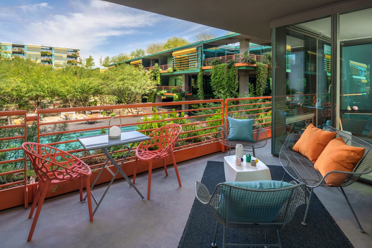 Optima Sonoran Village apartment balcony with colorful chairs, a small table, and cushions overlooking a modern apartment complex and lush greenery.
