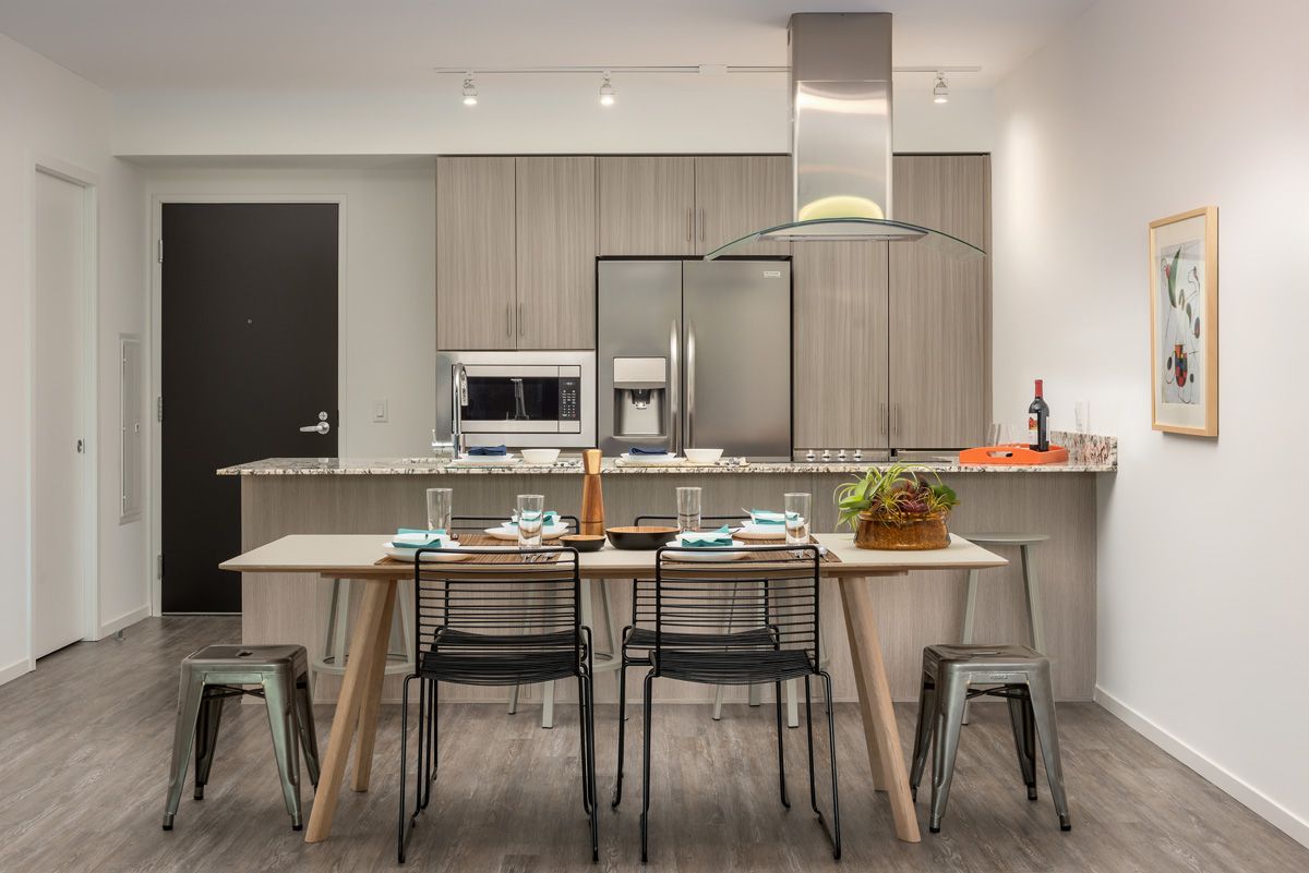 Optima Sonoran Village apartment Modern kitchen with dining table, chairs, barstools, stainless steel appliances, and a plant centerpiece.