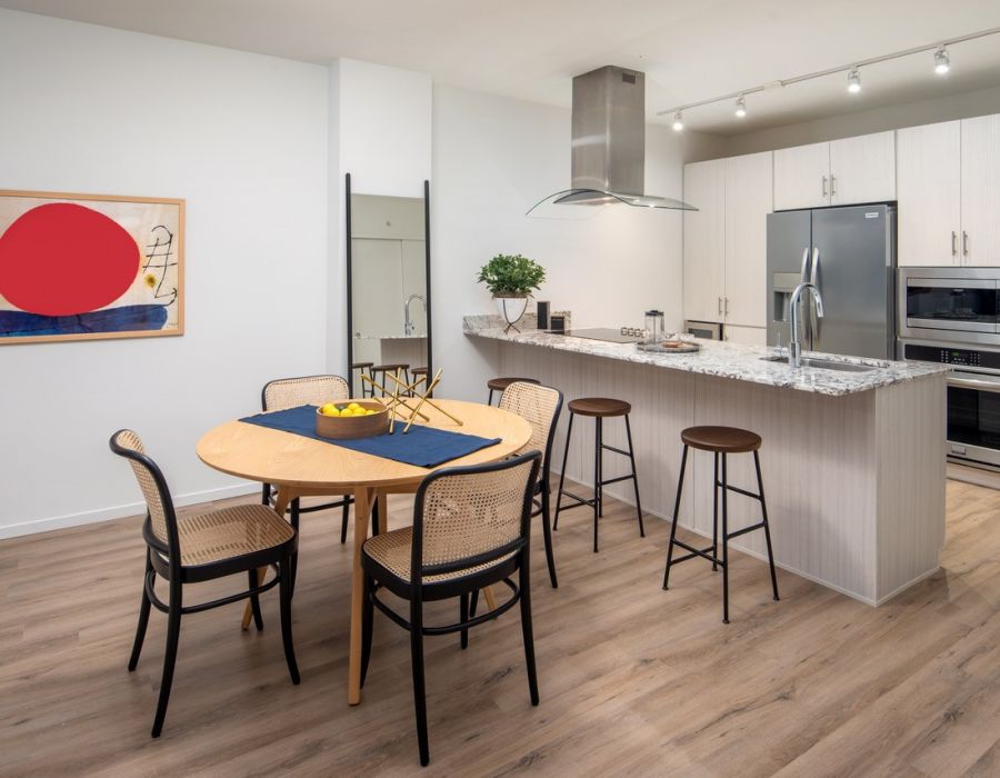Optima Sonoran Village apartments modern kitchen and dining area with wooden floors, a round table, bar stools, and stainless steel appliances.