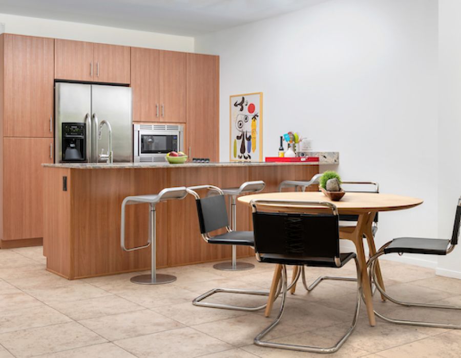 Optima Sonoran Village apartments modern kitchen with wooden cabinets and island, round dining table with four chairs, and wall art in background.